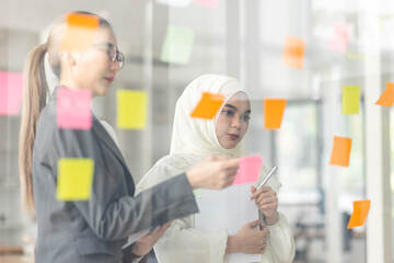 Young Asian woman Creative team use post it notes to share idea sticky note on glass wall. Asian...