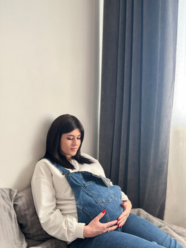 Waiting concept - happy woman at 9 months of pregnancy touching belly at home
