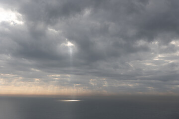 Naklejka na ściany i meble The sun rays breaking through gray clouds reflecting on the sea surface