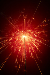 Close up of sparkler is burning, sparks emitting a red glow, standing out against a dark background. Scene of birthday party, happy new year and merry christmas. Front view