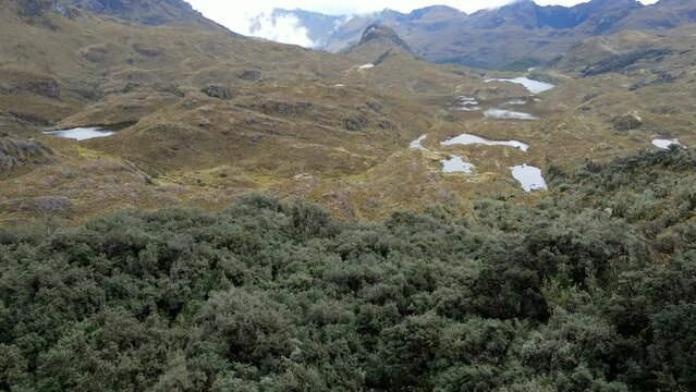 Aerial shot drone slowly ascends over a valley full of lakes surrounded by mountains on a cloudy day