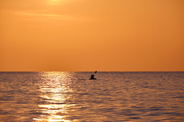 Fototapeta premium Dark silhouette of lonely fisherman rowing on his boat on sea water at sunset