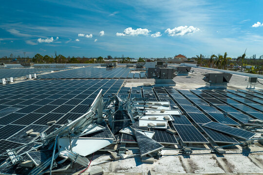 Top view of destroyed by hurricane Ian photovoltaic solar panels mounted on industrial building roof for producing green ecological electricity. Consequences of natural disaster in Florida