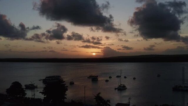 Trucking left aerial shot of the alligator beach, a river in Cabedelo, Paraiba, Brazil, near the coastal capital, Joao Pessoa, with tour boats watching the sunset as a man plays the saxophone below