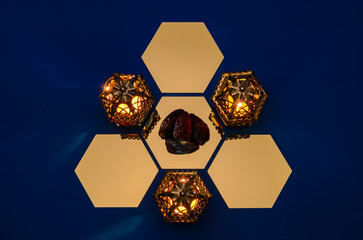 Selective focus on dates fruit with blurred lanterns put on golden mirror with blue background for...