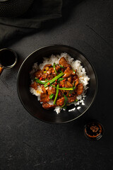 Asian cooked beef with spring onion and rice on black background