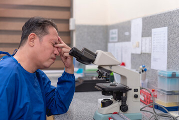 An asian male laboratory technician or microbiologist in his 40s feeling exhausted and burned out...