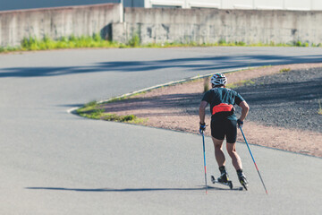 Athletes ride roller skis on asphalt track, group of ski rollers in helmet, cross-country skiing with roller ski in summer sunny day, sportsmen ski-rollers riding, biathlete training 