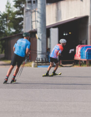 Athletes ride roller skis on asphalt track, group of ski rollers in helmet, cross-country skiing with roller ski in summer sunny day, sportsmen ski-rollers riding, biathlete training 