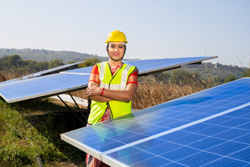 Portrait of Young indian woman technician wearing yellow hard hat standing near solar...