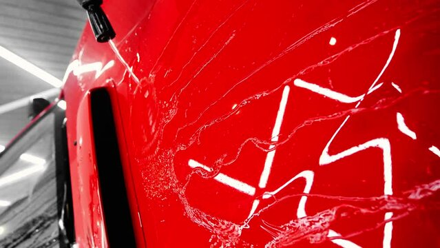 Man washes a red car, pouring water on the hood. Checking the layer of ceramic protective coating anti-rain. Car wash or car detailing process. Vertical video
