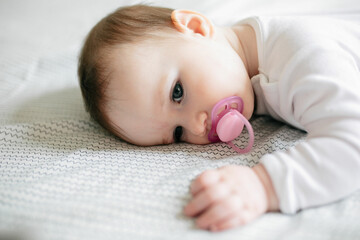 baby girl lying on bed with pink pacifier looking listless and unhappy