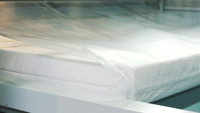 Close-up of a mattress being packaged in plastic wrap on a factory assembly line