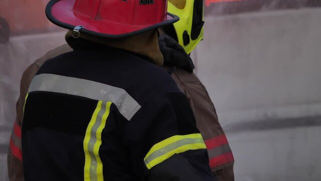 Rear view of Asian fireman wear fire protection suit. Firefighter fighting with fire on a car during fire drill Traffic Accident at Fire station Concept. Slow motion