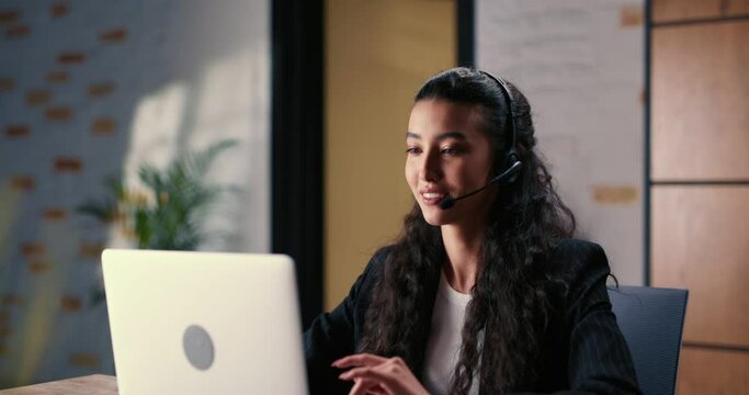 Burnt out from the monotonous work of a customer support hotline, a young multiethnic woman takes off her headphones, leans back in her chair and wearily closes her eyes to rest after hard day's work.