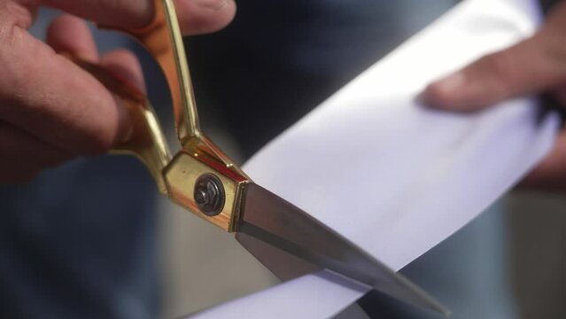 cutting a white ribbon with golden scissors at an opening event in 4k