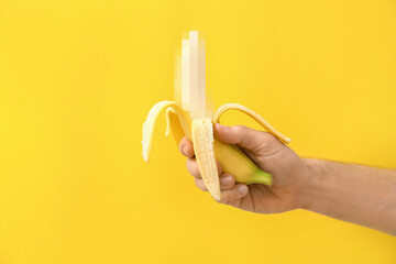 Male hand with banana on yellow background. Concept of sex education - obrazy, fototapety, plakaty