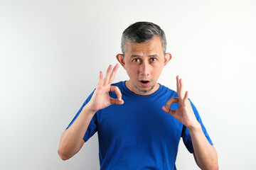 Asian handsome grey-haired man wearing blue tshirt over isolated white background smiling positive doing ok sign with hand and fingers. Successful expression.
