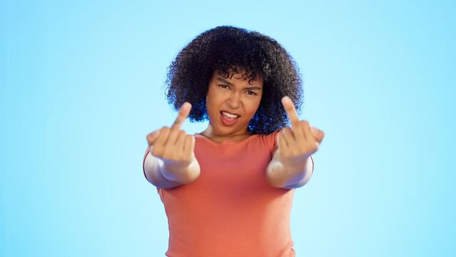 Black woman, angry and middle finger in studio for expression of conflict or offence on isolated on blue background. Fingers, rude hand gesture and offended or frustrated person with anger and hate.