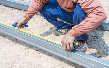Man workers' hands use measuring tape to measure the length of the steel part in homebuilding. Construction labor hands are using steel tape to measure the length of the steel