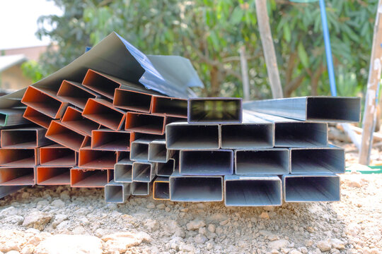 Group of square steel rectangle tubes metal iron production profiles pipe on the ground. Square metal pipes for background using metal pipes and rods, steel materials, building materials.
