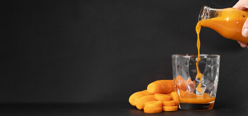 Freshly squeezed carrot juice in a glass bottle pouring into glass on black textured background....