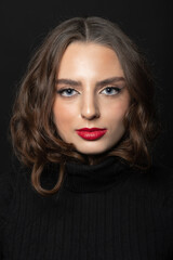 Fototapeta premium Beauty concept. Brunette woman with long wavy hair, nude make-up and red lipstick close-up studio portrait. Model looking at camera with seductive blue eyes. Wearing black turtle neck sweater
