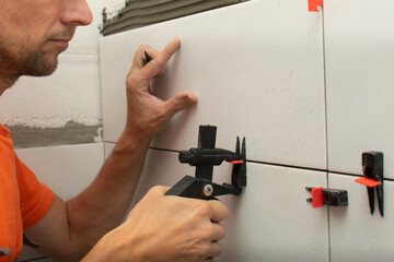Builder glues tiles on the wall, tile leveling system