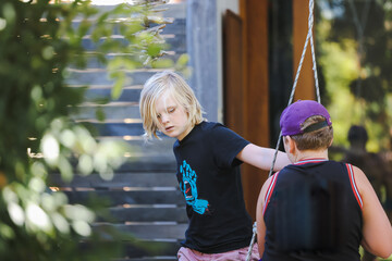 Two brothers playing together on backyard swing on bright spring day