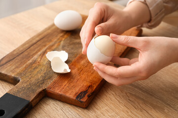 Fototapeta na wymiar Woman peeling boiled egg at wooden table, closeup