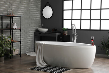 Bathtub with wine glass and candle in interior of modern bathroom