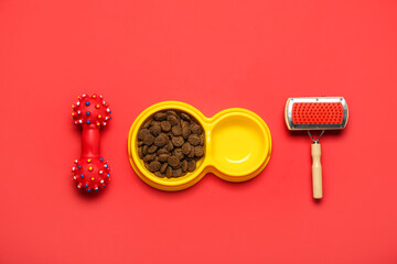 Obraz na płótnie Canvas Bowl of dry pet food, grooming brush and rubber toy on red background
