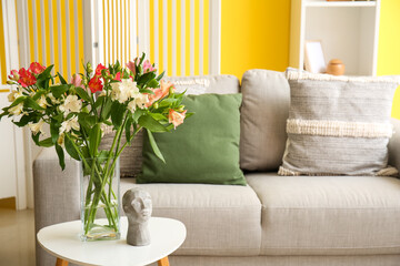 Interior of living room with cozy sofa and alstroemeria flowers on table