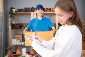 The girl signs the clipboard document before picking up the items from the man, who is holding the products in a cardboard box in his hand.