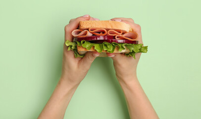 Female hands holding delicious ham sandwich on green background
