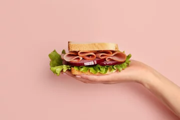 Foto op Plexiglas anti-reflex Female hand holding delicious ham sandwich on pink background © Pixel-Shot