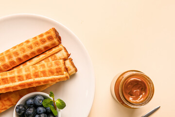 Plate of delicious wafer rolls with blueberries and boiled condensed milk on beige background