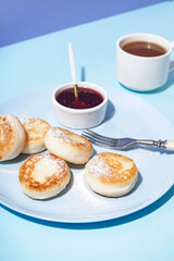 Plate with tasty cottage cheese pancakes, strawberry jam and cup of coffee on color background, closeup