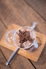 Fototapeta premium Iced chocolate with chocolate chunks on ice in a glass on a wooden coaster
