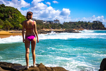 A beautiful girl in a pink bikini stands on a rock and enjoys the paradise scenery of small bays with golden sand and turquoise ocean in Sunshine Coast. Hidden gems in Queensland, Australia