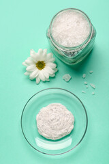 Bowl of body scrub, jar with sea salt and chamomile flower on color background