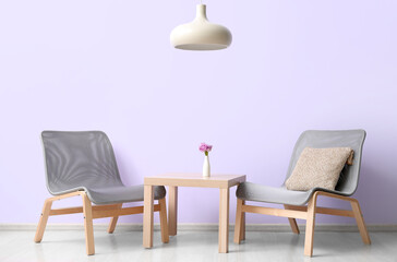Fototapeta na wymiar Stylish grey armchairs and table near lilac wall
