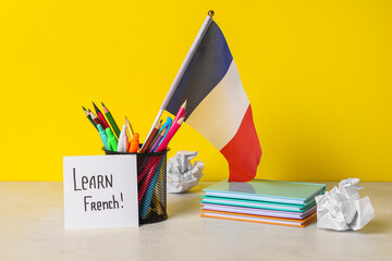 Paper with text LEARN FRENCH, flag and stationery on table near yellow wall