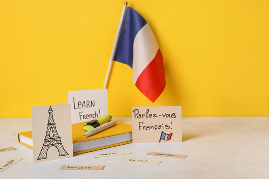 Paper with text LEARN FRENCH, drawn Eiffel Tower, flag and stationery on table near yellow wall