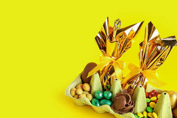 Holder with chocolate Easter eggs and candies on yellow background