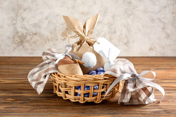 Basket with Easter eggs and bunny gift bag on wooden table against grunge wall
