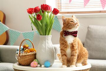 Cute cat, vase with tulips and Easter eggs on table at home