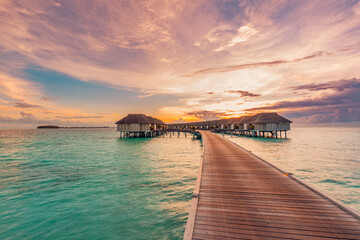 Amazing beach panoramic landscape. Beautiful Maldives sunset seascape view. Horizon colorful sea sky clouds, over water villa pier pathway. Tranquil island lagoon, vacation travel panorama background
