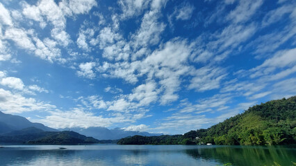 Sun Moon Lake in Nantou, Taiwan is a beautiful scenery which mountains surrounding a lake like mirror with white clouds in the blue sky.