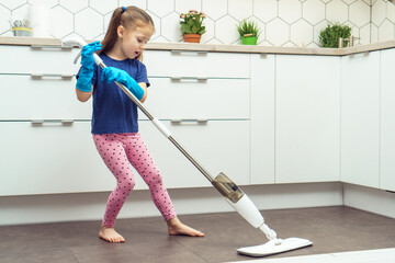 Pretty little girl in household gloves wash floor with modern mop with removable brush near kitchen...